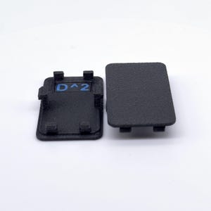 May include: Two black plastic keycaps, one with the text "D^2" in blue lettering, and the other blank.