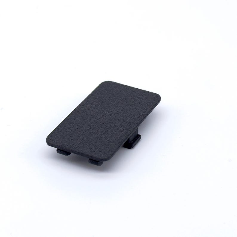 May include: A black plastic cover with a textured surface. The cover has two small tabs on each side.
