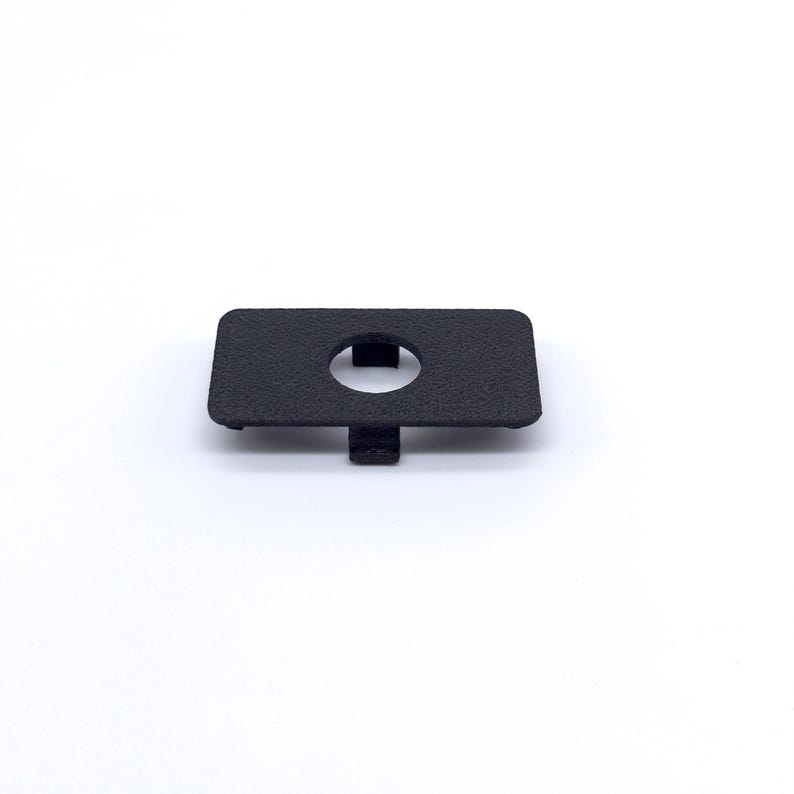 May include: A black plastic cover with a round hole in the center. The cover has a textured surface.