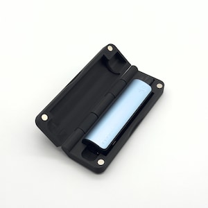 Puede incluir: Un estuche negro abierto con un dispositivo electrónico azul claro en su interior. El dispositivo tiene la palabra "CLIQ" impresa. El estuche es articulado y tiene cierres magnéticos. El estuche está diseñado para proteger el dispositivo.