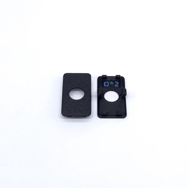 May include: Two black plastic pieces with a round hole in the center. One piece has the text "D^2" printed on it.