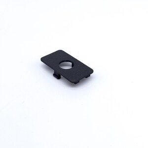 May include: A black plastic cover with a round hole in the center. The cover has a textured surface.