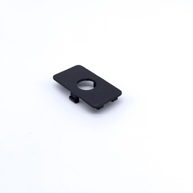 May include: A black plastic cover with a round hole in the center. The cover has a textured surface.