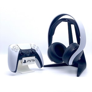 Könnte beinhalten: Ein weißer PlayStation 5 Controller mit einem schwarzen Ständer und ein weißes PlayStation 5 Headset mit einem schwarzen Ständer. Das Headset hat ein schwarz-weißes Design mit dem PlayStation-Logo an der Seite.