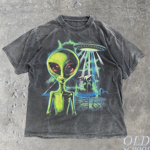 Puede incluir: Una camiseta gris carbón de manga corta con un estampado gráfico de un gran alienígena verde con ojos rojos. Sobre el alienígena, un platillo volante emite un haz de luz sobre una vaca en un campo. El texto "OLD SCHOOL CULT" está impreso en la esquina inferior derecha.