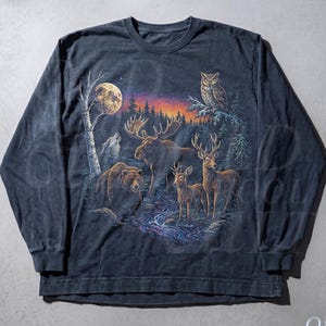 Puede incluir: Camiseta de manga larga azul medianoche con una escena de bosque con un lobo, un oso, un alce, ciervos y un búho bajo la luna llena. La camiseta tiene un aspecto vintage y descolorido con el texto "OLD SCHOOL CULT" y "Midnight".