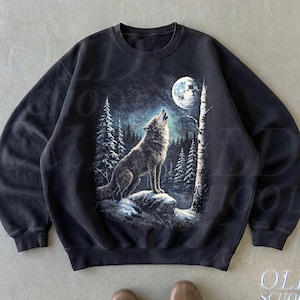 Pode incluir: Uma camisola preta de gola redonda com uma impressão gráfica de um lobo a uivar para a lua cheia num cenário de floresta. O design inclui pinheiros altos, uma rocha texturada e um tronco de bétula. O texto OLD SCHOOL CULT é visível.