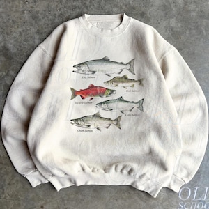 Op de afbeelding: Een zandkleurige sweater met ronde hals en een grafische print van vier verschillende zalmsoorten. De vissen zijn gelabeld als King Salmon, Pink Salmon, Sockeye Salmon en Chum Salmon, waarbij de Sockeye Salmon in het rood is afgebeeld.