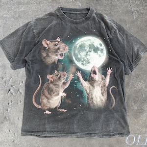 May include: A charcoal grey short-sleeve t-shirt featuring a graphic print of three brown rats reaching towards a large, bright full moon against a dark, starry background. The shirt has a crew neckline and a faded, washed-out fabric appearance.