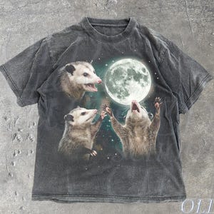Puede incluir: Camiseta gris oscuro con un diseño de tres zarigüeyas adorando una luna llena. La camiseta tiene un aspecto vintage y desgastado. El texto "OLD SCHOOL CULT" está impreso en la esquina inferior derecha y la palabra "Pepper" en la inferior izquierda.