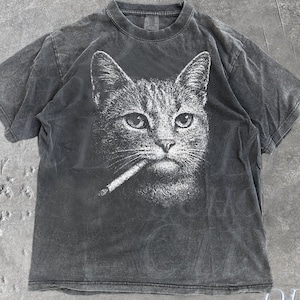 May include: Dark grey t-shirt with a white graphic of a cat smoking a cigarette. The shirt has a faded, vintage look. The text "Pepper" is at the bottom left, and "OLD SCHOOL CULT" is at the bottom right.