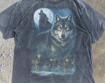 Può includere: T-shirt grigio scuro con un disegno di un branco di lupi sotto la luna piena. La grafica presenta un lupo grande e diversi più piccoli. Il testo "OLD SCHOOL CULT" è stampato sulla maglietta. La parola "Denim" è anche visibile.
