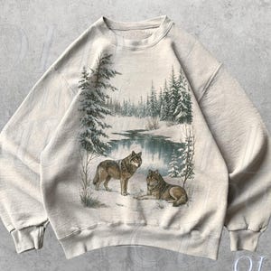 May include: Sand-coloured sweatshirt with a winter scene featuring two wolves. The graphic shows a snowy landscape with a river and evergreen trees. The text "OLD SCHOOL CULT" is printed on the bottom right.