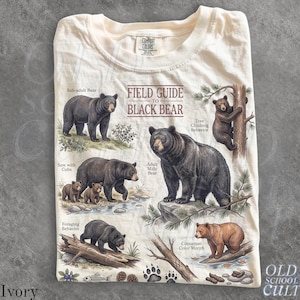 Peut inclure: Un t-shirt ivoire avec une impression graphique intitulée Field Guide to Black Bear. Le motif comprend des illustrations d'ours noirs dans divers environnements avec des étiquettes comme Sub-adult Bear, Sow with Cubs, Adult Male Bear et Cinnamon Color Morph.