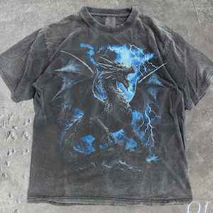 May include: A dark grey t-shirt with a dragon illustration and blue lightning. The dragon is the central image, with blue electric bolts surrounding it. The text "OLD SCHOOL CULT" is visible. The shirt has a vintage look.