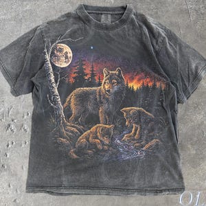 以下が含まれることがあります： 満月の下でオオカミの群れが描かれたグレーのTシャツ。グラフィックには、小川の近くにいるオオカミと2匹の子オオカミ、背景に森と夕焼けが含まれています。シャツには「Old School Cult」と「Pepper」の文字が入っています。