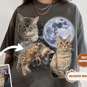 May include: Dark grey t-shirt with a design of three cats, a full moon, and a starry background. The shirt includes a small image of a cat and the words "UNLIMITED PROOFS" and "FAST SHIPPING".