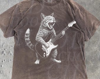 May include: Espresso-colored t-shirt featuring a detailed graphic of a cat playing an electric guitar. The cat is depicted with its mouth open, as if singing. The shirt has a vintage, distressed look, with the words "OLD SCHOOL CULT" printed on the bottom right.
