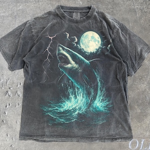 May include: Dark grey t-shirt featuring a shark leaping from the water under a full moon. The graphic includes lightning and the text "OLD SCHOOL CULT". The shirt has a vintage, distressed look.