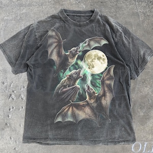 May include: Dark grey t-shirt with a graphic of three bats with outstretched wings, howling at a full moon. The design includes green and white accents. The text "OLD SCHOOL CULT" is printed on the bottom right.