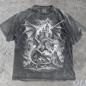 May include: A grey t-shirt with a dragon and castle graphic. The design is in shades of grey and white, with lightning in the background. The text "OLD SCHOOL CULT" is printed on the bottom right. The t-shirt is pepper-colored.