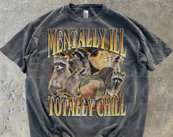 May include: A grey t-shirt with a graphic print of raccoons and a capybara. The text "Mentally Ill Totally Chill" is printed in yellow on the shirt.