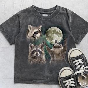 May include: Vintage grey t-shirt featuring a graphic of three raccoons and a full moon. One raccoon is looking up at the moon with its arms raised. The text "OLD SCHOOL CULT" is visible on the right side of the image.