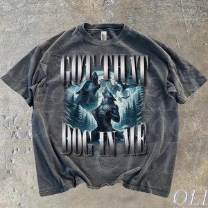 May include: A gray t-shirt with a graphic of two wolves howling at the moon. The text "GOT THAT DOG IN ME" is printed in silver on the shirt.