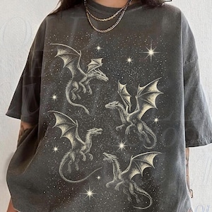 May include: Dark gray t-shirt featuring a celestial design with four dragons and stars. The dragons have detailed wings and are in various poses. The shirt has a vintage, faded look. The text "OLD SCHOOL CULT" is visible on the bottom right.