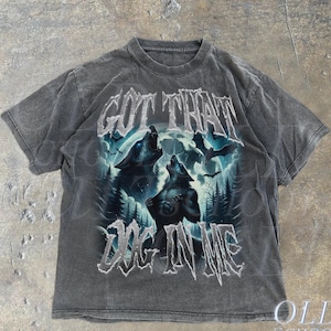 K&ouml;nnte beinhalten: Ein graues T-Shirt mit Used-Look, das ein Motiv mit zwei W&ouml;lfen zeigt, die zum Mond heulen, mit dem Text "GOT THAT DOG IN ME" auf der Vorderseite.