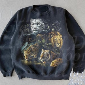 Puede incluir: Sudadera negra de cuello redondo con una ilustración detallada de grandes felinos: leopardo de las nieves, león, jaguar, tigre y pantera negra. La sudadera tiene un aspecto vintage y descolorido con el texto "OLD SCHOOL CULT" y "Black".
