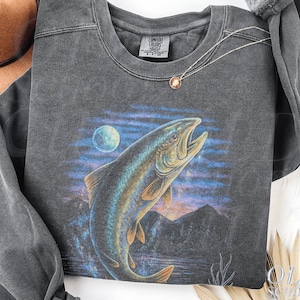 May include: Dark grey sweatshirt with a leaping fish graphic, moon, and mountain scene. The crew neck sweatshirt has long sleeves. The brand tag is visible on the neckline. The text "OLD SCHOOL CULT" is printed on the bottom right.