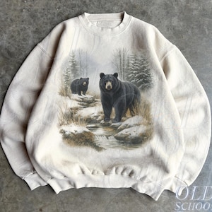 May include: Sand-colored sweatshirt featuring a detailed graphic of two black bears in a snowy forest scene. The bears stand near a stream, with trees in the background. The text "OLD SCHOOL CULT" is printed on the lower right.