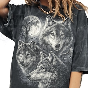 May include: Dark gray t-shirt featuring a detailed graphic of three wolves with a full moon and bare tree silhouette in the background. The design is in shades of gray and black, creating a vintage, distressed look.
