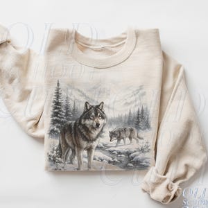 May include: Sand-coloured sweatshirt with a detailed illustration of two wolves in a snowy forest landscape. The design includes a river, pine trees, and mountains. The sweatshirt has a crew neck and long sleeves.