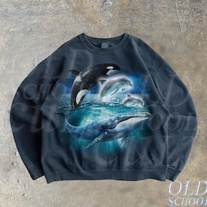 Puede incluir: Sudadera negra con un estampado gráfico de una ballena, una orca y delfines saltando fuera del agua. El gráfico está en tonos de azul y blanco.