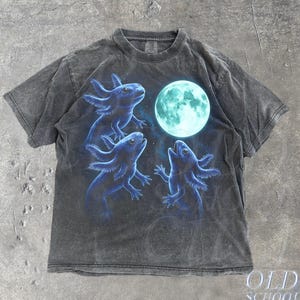 Könnte beinhalten: Dunkelgraues T-Shirt mit einem Design aus drei blauen Axolotln und einem leuchtenden türkisfarbenen Mond. Das Shirt hat ein Vintage-Aussehen. Der Text "OLD SCHOOL CULT" ist unten rechts aufgedruckt.