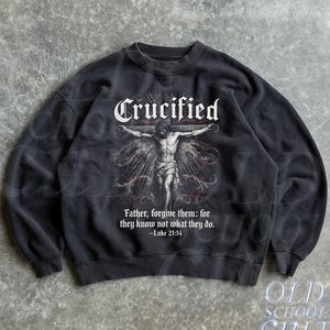 Puede incluir: Sudadera negra con un gráfico de una figura crucificada y la palabra "Crucified" arriba. El texto "Father, forgive them: for they know not what they do. -Luke 23:34" está impreso debajo. La sudadera también tiene el texto "OLD SCHOOL CULT".