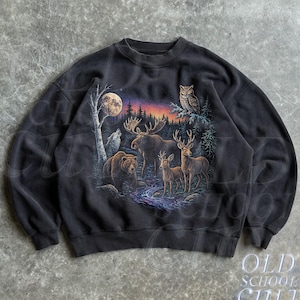 Könnte beinhalten: Schwarzes Sweatshirt mit Rundhalsausschnitt und einer Wildtierszene mit Bär, Elch, Hirsch, Wolf und Eule unter Vollmond. Die Grafik zeigt einen Fluss und einen Wald mit Sonnenuntergangsfarben. Der Text "OLD SCHOOL CULT" ist unten rechts aufgedruckt.