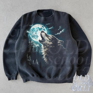 Puede incluir: Sudadera gris oscuro con un lobo aullando a la luna llena. El diseño presenta una ilustración detallada de un lobo, una luna azul brillante y una silueta de bosque. La sudadera tiene cuello redondo y mangas largas.