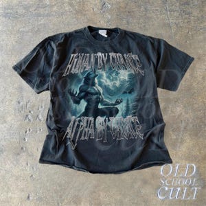 Puede incluir: Camiseta gris oscuro con un gr&aacute;fico de hombre lobo y el texto "HUMAN BY CHANCE" y "ALPHA BY CHOICE". El dise&ntilde;o incluye una escena de bosque con un lobo aullando. La camiseta tiene un aspecto vintage y las palabras "OLD SCHOOL CULT" est&aacute;n en la parte inferior.
