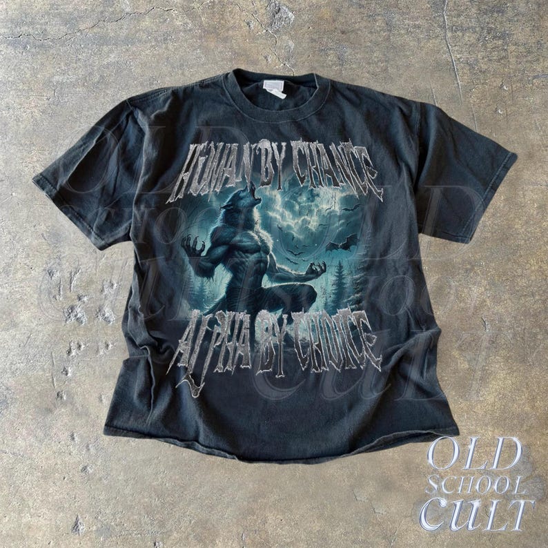 Puede incluir: Camiseta gris oscuro con un gr&aacute;fico de hombre lobo y el texto "HUMAN BY CHANCE" y "ALPHA BY CHOICE". El dise&ntilde;o incluye una escena de bosque con un lobo aullando. La camiseta tiene un aspecto vintage y las palabras "OLD SCHOOL CULT" est&aacute;n en la parte inferior.