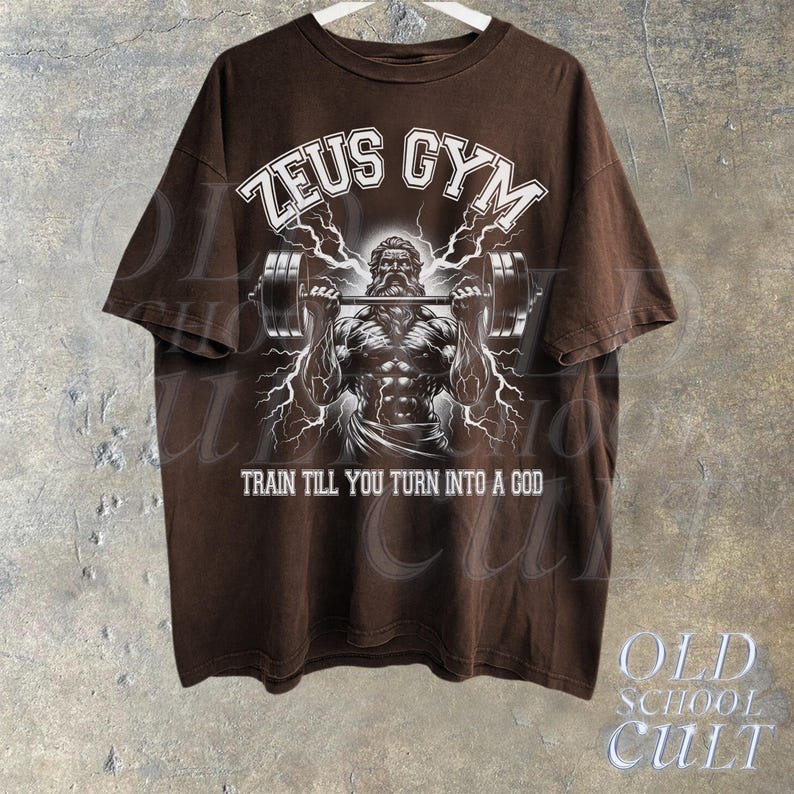 May include: Brown t-shirt with a white graphic of Zeus lifting weights. The graphic includes the text "Zeus Gym" and "Train till you turn into a god".