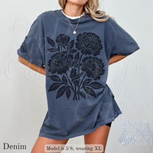 May include: Denim blue oversized t-shirt with a black floral design. The shirt has short sleeves and a crew neck. The text "Denim" is at the bottom left. The model is 5'8" and wearing XL.