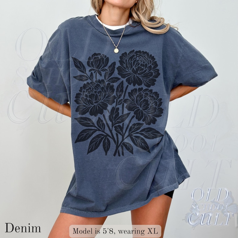 May include: Denim blue oversized t-shirt with a black floral design. The shirt has short sleeves and a crew neck. The text "Denim" is at the bottom left. The model is 5'8" and wearing XL.