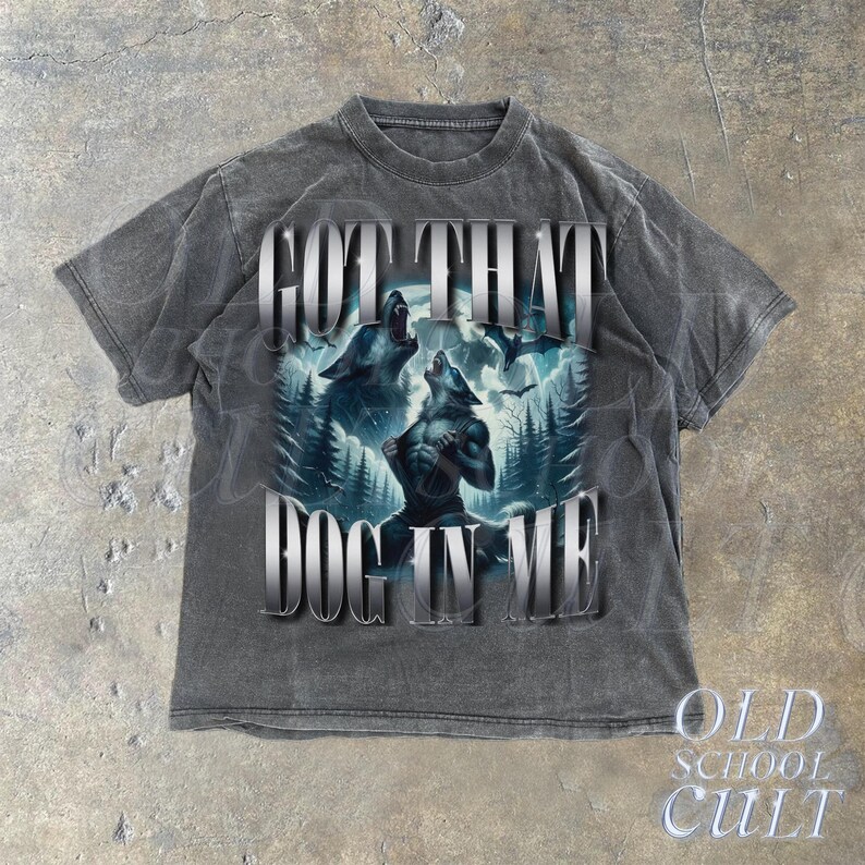 May include: A gray t-shirt with a distressed look features a graphic of two wolves howling at the moon. The text "GOT THAT DOG IN ME" is printed in silver lettering.