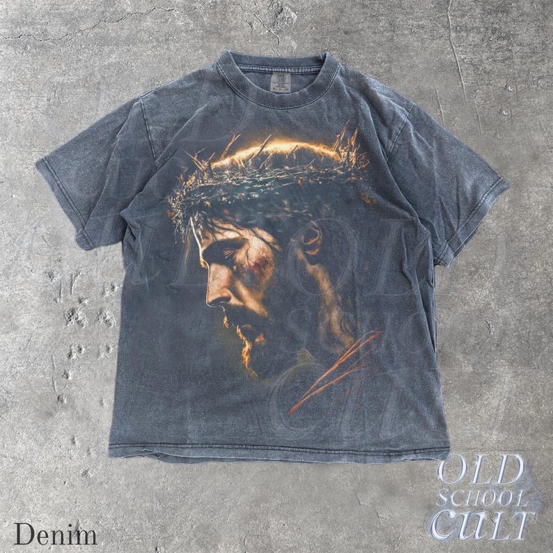 May include: Denim-colored t-shirt featuring a detailed portrait of a man with a beard and a crown of thorns. The graphic is in shades of brown, gold, and red. The text "OLD SCHOOL CULT" is printed in white. The word "Denim" is printed in white.