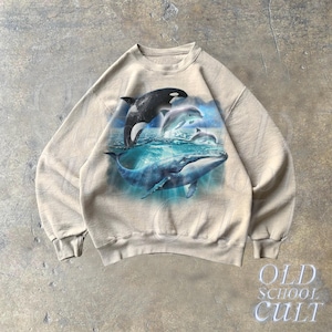 May include: A beige sweatshirt with a graphic print of a whale and dolphins swimming in the ocean. The graphic is in shades of blue, black, and white.