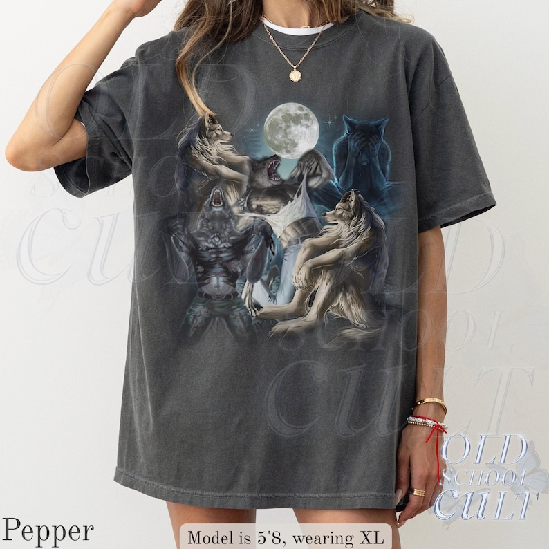 May include: Dark gray t-shirt featuring a graphic of wolves and a werewolf under a full moon. The design includes various wolf poses and a detailed illustration style. The shirt has a vintage, worn look.