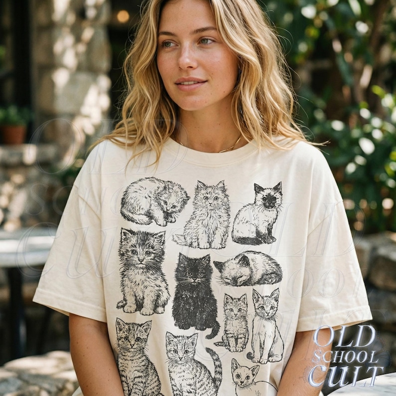 May include: Cream-colored t-shirt featuring a collection of black and white cat illustrations. The cats are depicted in various poses, including sitting, sleeping, and standing. The text "OLD SCHOOL CULT" is printed in a stylized font on the lower right.